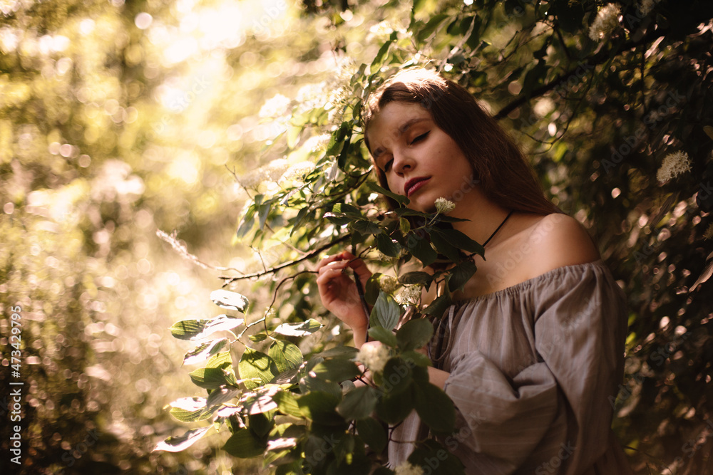 Peaceful young woman standing by flowering branches in park in summer Peaceful young woman standing by flowering branches in park in summer