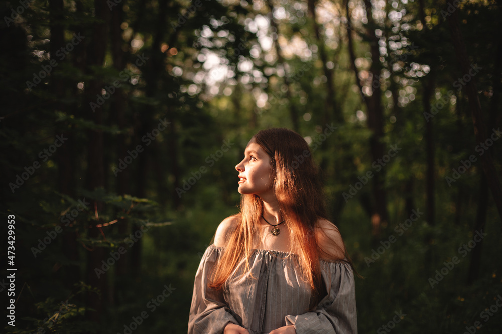 Young woman looking at sunlight while standing in dark forest Young woman looking at sunlight while standing in dark forest