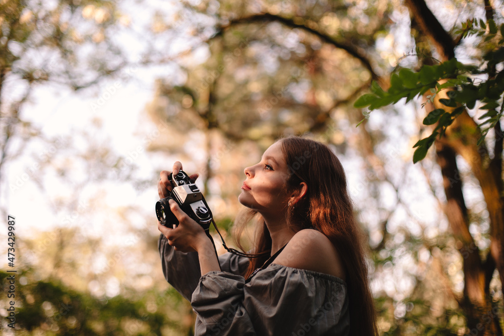 Young woman photographing with camera while standing in summer forest Young woman photographing with camera while standing in summer forest