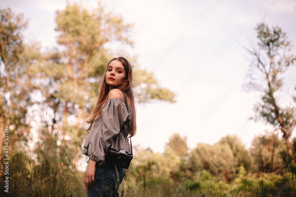 Young woman with camera standing in forest during summer Young woman with camera standing in forest during summer