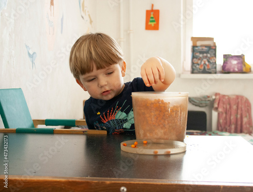 Foto Todler blond boy eats a berry at a table at home.