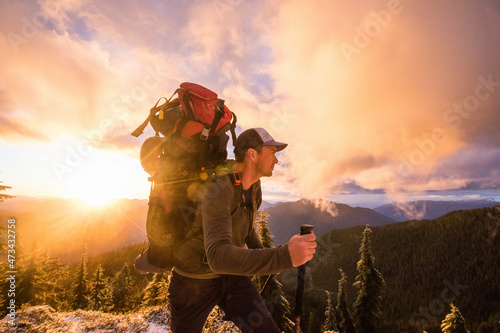 Side view of man backpacking on mountain ridge with scenic view.