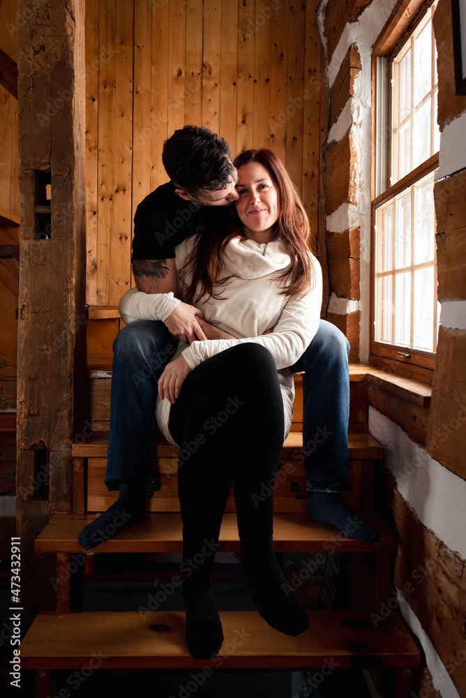 Attractive couple sitting on stairs together inside rustic log cabin. Attractive couple sitting on stairs together inside rustic log cabin.