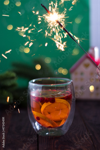 christmas cocktail on a wooden table with a green background and lights and a glowing house with a sparkler