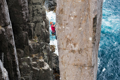 Adventurous man rockclimbs an exposed rock column with sea cliffs and the ocean in the background in The Totem Pole, Cape Hauy, Tasman National Park, Tasmania, Australia. photo