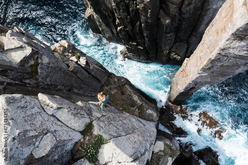 Adventurous woman smiles as she rappels down from the edge of a sea cliff to the bottom of the Totem Pole, a rock column which emerges out of the ocean in Cape Hauy, Tasmania photo