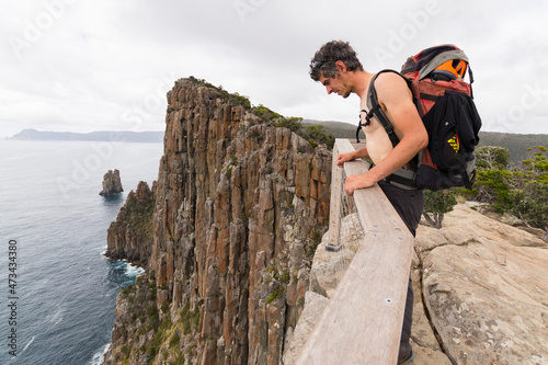 Man carrying a backpack leans over the top of sea cliff in Tasmania. photo