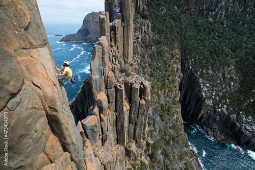 Young man climbs the exposed edge of a rock ridge of columns along sea cliffs which emerge out of the ocean in Cape Raoul, Tasmania, Australia. photo