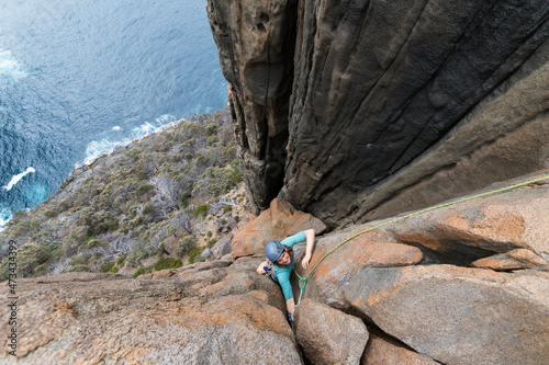 Female adventurer and rockclimber makes her way up the dolerite sea cliffs of Cape Raoul, Tasmania, Australia. photo
