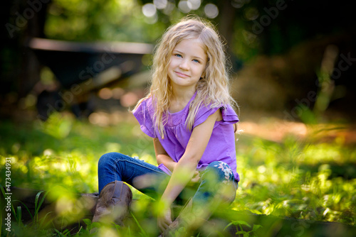 Beautiful little blond girl in purple shirt sitting on the grass. photo