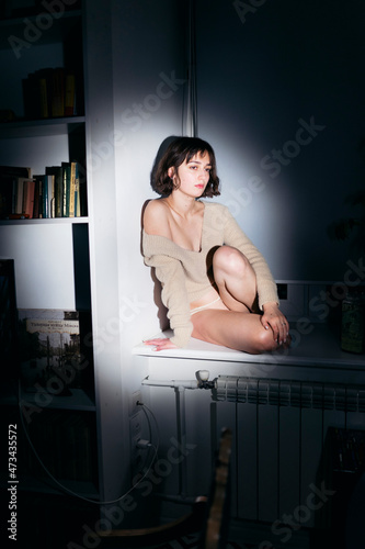 a woman sits on the windowsill in the evening in panties