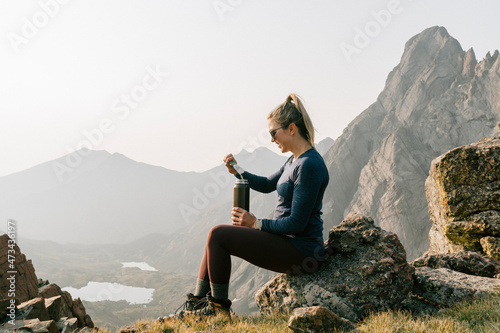 Side view of woman having energy drink while sitting on mountain against clear sky photo