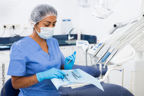 Focused female dentist preparing to receive patients in dental office, checking and arranging tools