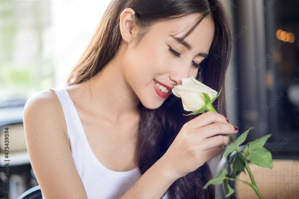 Young beautiful Asian woman holding a white rose in Valentine’s Day and enjoying its smell Young beautiful Asian woman holding a white rose in Valentine’s Day and enjoying its smell