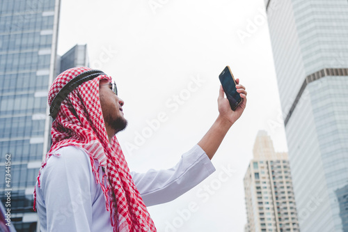 Islamic man using smartphones app organize schedule agenda  focus on hands holding smartphone muslim modern uae city. Arab men wear hijab and muslim formal dress sending text sms online lifestyle photo