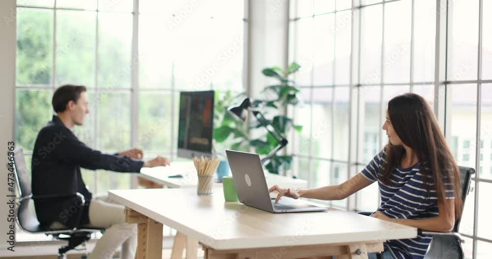 Caucasian young wife freelancer in casual outfit sitting typing working with laptop computer while happy funny husband listening to fast rhythm music standing dancing around workplace in home office