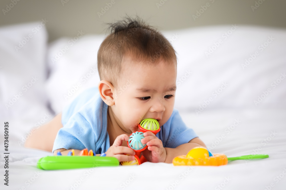 Adorable and innocent little Asian baby enjoys playing fun with colorful children toy while lying on stomach on bed. Adorable and innocent little Asian baby enjoys playing fun with colorful children toy while lying on stomach on bed.