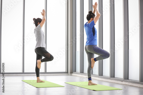 Healthy and strong women excercise yoga activity on fitness mat by practicing tree pose to train body balancing and strength by one leg standing with hands above head at indoor sport gym.
