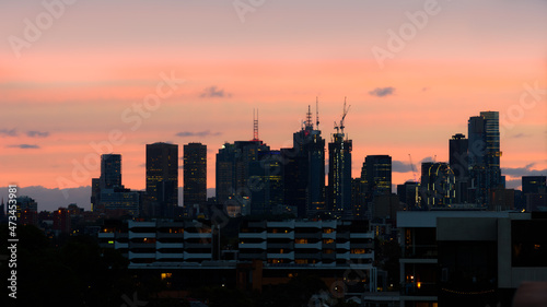 Melbourne, Australia city skyline at dusk or early sunset showing buildings, clouds and trees in the foreground.