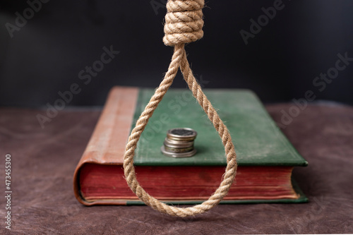 Fotografia hangman noose over an old book cover with a stack of coins, on a dark background