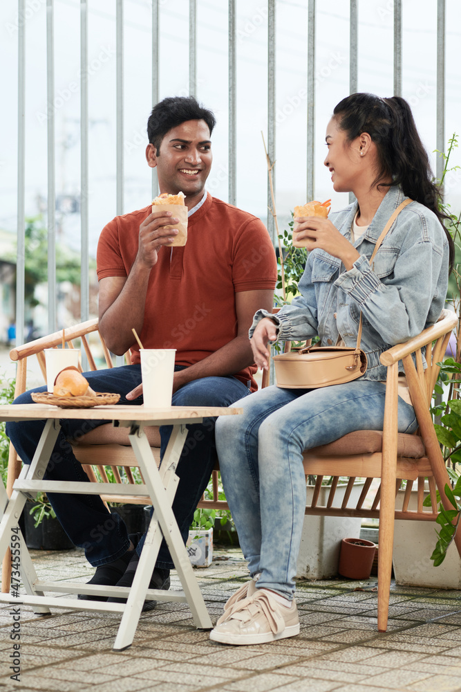 Happy diverse young couple enjoying street food and good talk when spending date outdoors