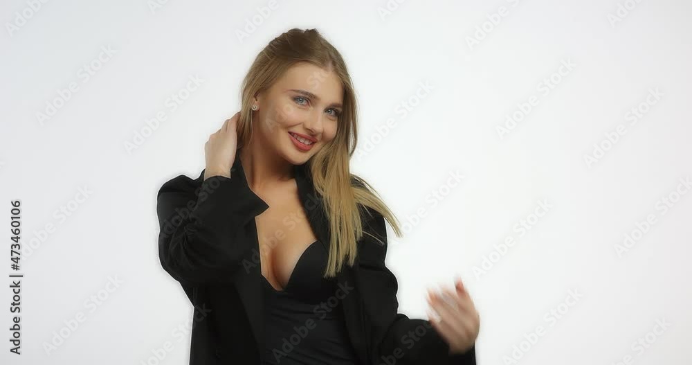 Beautiful young woman posing while sitting on a chair in the studio at the camera on a white background. A model Caucasian girl with long blond hair in a black shirt is smiling. Beautiful female face. Beautiful young woman posing while sitting on a chair in the studio at the camera on a white background. A model Caucasian girl with long blond hair in a black shirt is smiling. Beautiful female face.