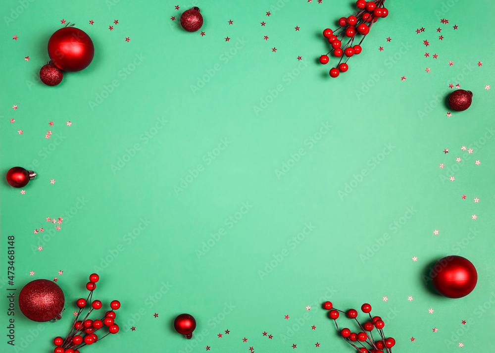 Christmas frame of red decorations and berries on green background.