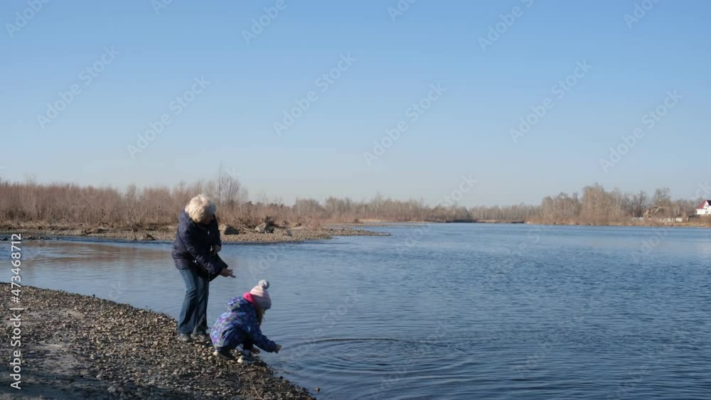 Grandmother and grandchild throws stones into the river. Activity outdoors Grandmother and grandchild throws stones into the river. Activity outdoors