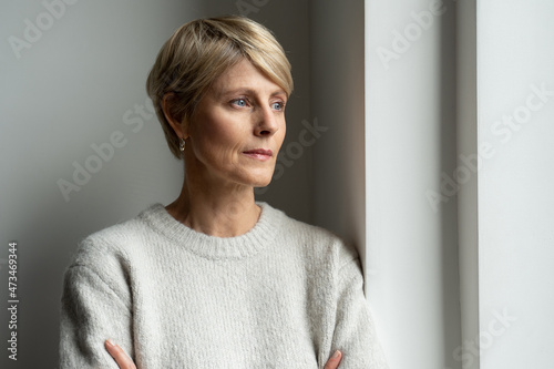 A thoughtful middle-aged woman looks out the window and is sad