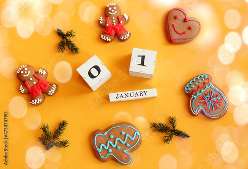 Calendar for January 1: cubes with numbers 0 and 1, the name of the month in English among gingerbread in the form of men, hearts, mittens and fir branches, yellow background, top view, bokeh photo