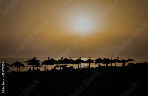 Silhouette of sun umbrellas and people on beach during sunset. In Almeria, Spain