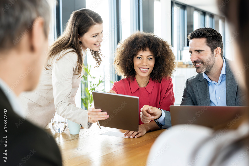 Smiling businesswoman attending meeting with colleagues in office Smiling businesswoman attending meeting with colleagues in office