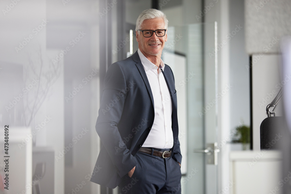Smiling businessman with hands in pockets standing at office Smiling businessman with hands in pockets standing at office