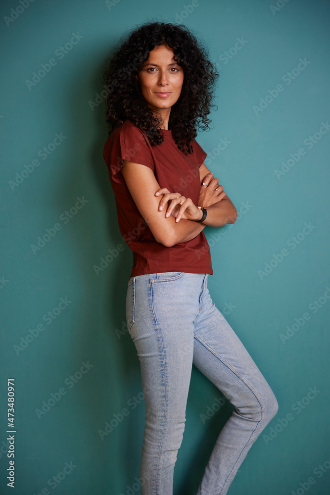Confident woman with arms crossed leaning on turquoise wall Confident woman with arms crossed leaning on turquoise wall