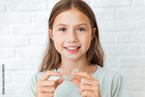 Smiling child girl with perfect and healthy teeth using removable braces or aligner for straightening and whitening teeth. Orthodontic treatment for correction of bite
