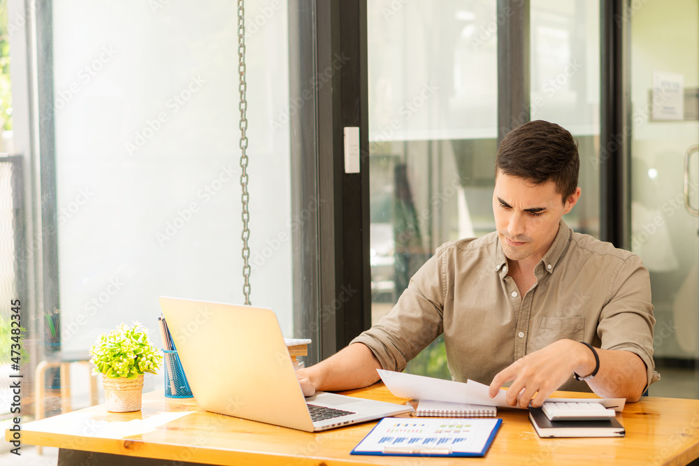 Fototapeta premium young businessman looking at market research report Analyze statistical data in charts. Develop a growth strategy Work on a computer alone in a modern office