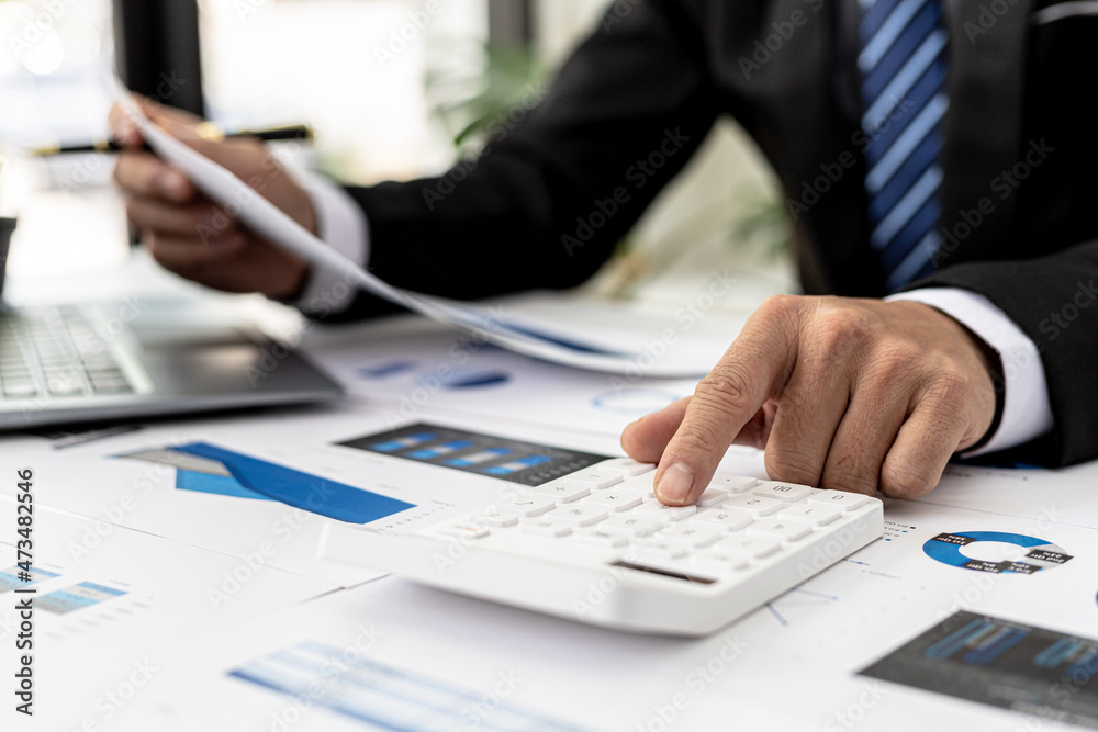 Businessman using a calculator to calculate numbers on a company's financial documents, he is analyzing historical financial data to plan how to grow the company. Financial concept. Businessman using a calculator to calculate numbers on a company's financial documents, he is analyzing historical financial data to plan how to grow the company. Financial concept.