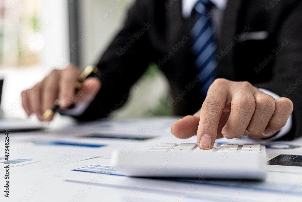 Businessman using a calculator to calculate numbers on a company's financial documents, he is analyzing historical financial data to plan how to grow the company. Financial concept. Businessman using a calculator to calculate numbers on a company's financial documents, he is analyzing historical financial data to plan how to grow the company. Financial concept.