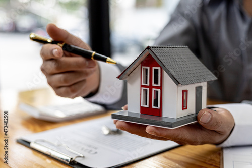 Salesman holding an orange model of a small house, a housing project salesman is drafting a sales contract for a customer who reserves a house in a project he maintains. Real estate trading concept.