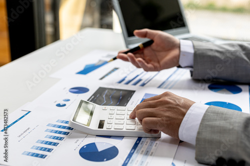 Businessman using a calculator to calculate numbers on a company's financial documents, he is analyzing historical financial data to plan how to grow the company. Financial concept.