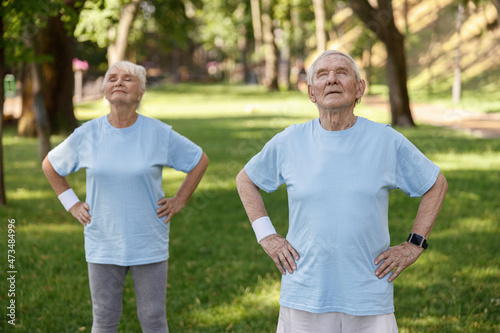 Positive mature man and woman do yoga on lush lawn in park