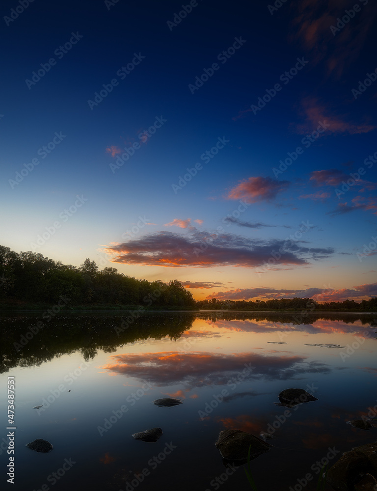 The sky with clouds during sunset is reflected in the water of the river.