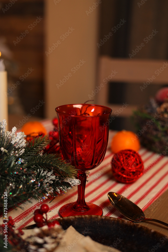 Festive decoration of the New Year's table, serving dishes for New Year's dinner, cones, tangerines, fir branches, garlands, candles and glasses, bokeh on the background. The concept of Christmas