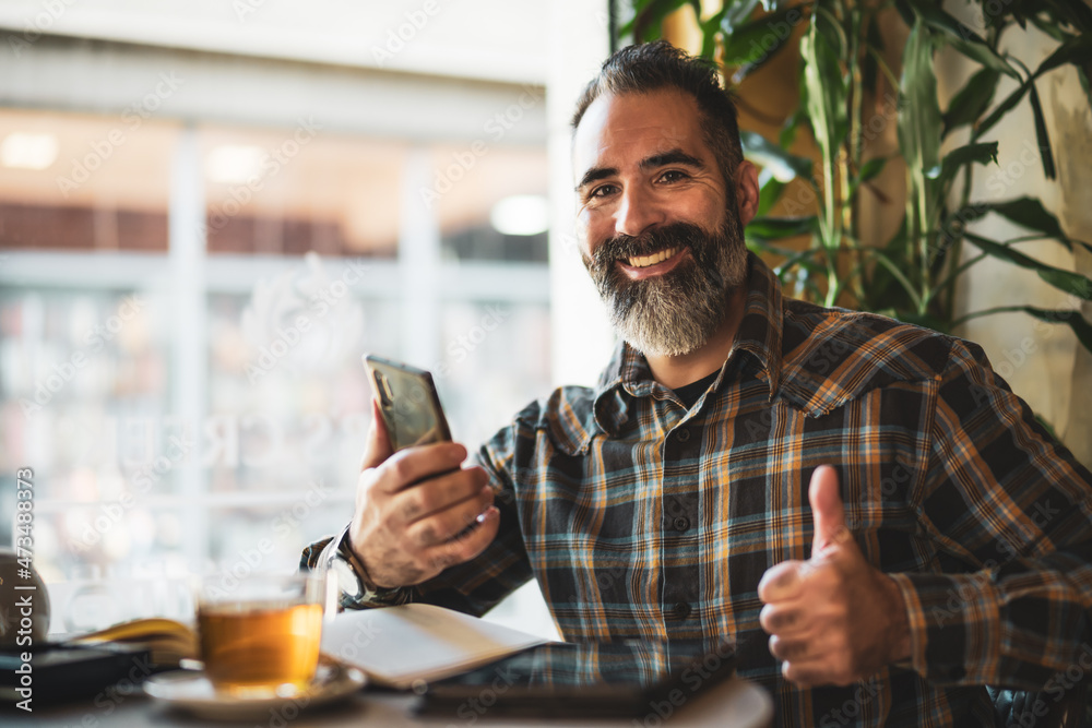 Adult man is sitting in cafe and making his daily schedule. He is using smartphone and note pad. Adult man is sitting in cafe and making his daily schedule. He is using smartphone and note pad.