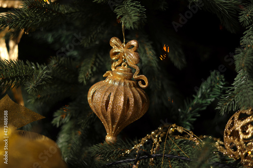 Golden Christmas toy hanging on the Christmas tree. Golden bokeh lights on a festive background. The concept of home comfort and festive mood. Decorate the Christmas tree © Ксения Третьякова