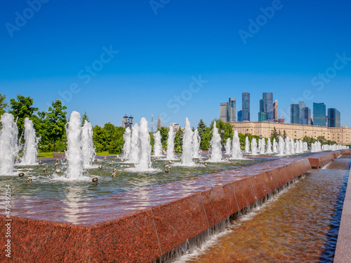 Jets of fountains on a sunny day against the backdrop of modern skyscrapers and a cloudless blue sky. Recreation area in Victory Park on Poklonnaya Hill in summer.