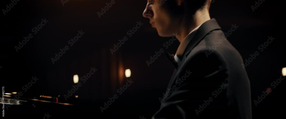 PORTRAIT of Young 20s aspiring musician playing grand piano on a stage of a huge concert hall. Shot with 2x anamorphic lens