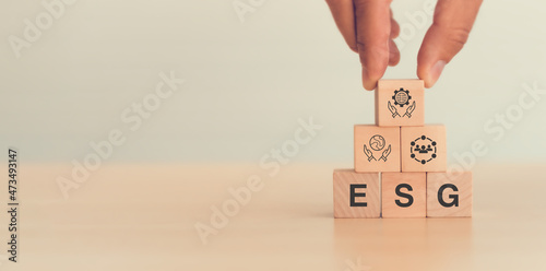 ESG concept of environmental, social and governance. Sustainable, ethical business. Businessman holds wooden cube with governance icon. Text "ESG", other ESG icon on white background and copy space.