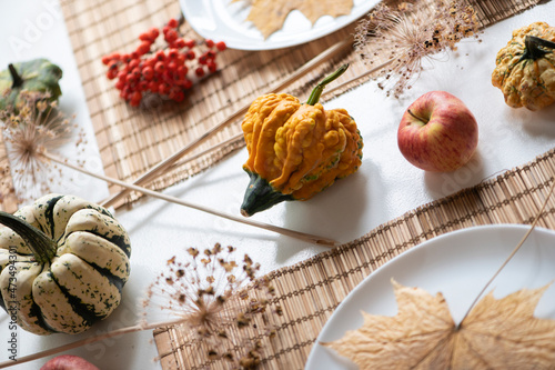 flat lay of small pumpkins and dry brown maple leafs on white plates, autumn dinner table decors