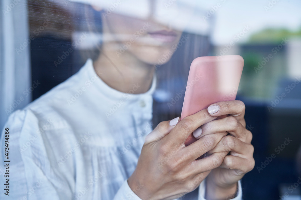 Woman using smart phone at home seen through glass Woman using smart phone at home seen through glass